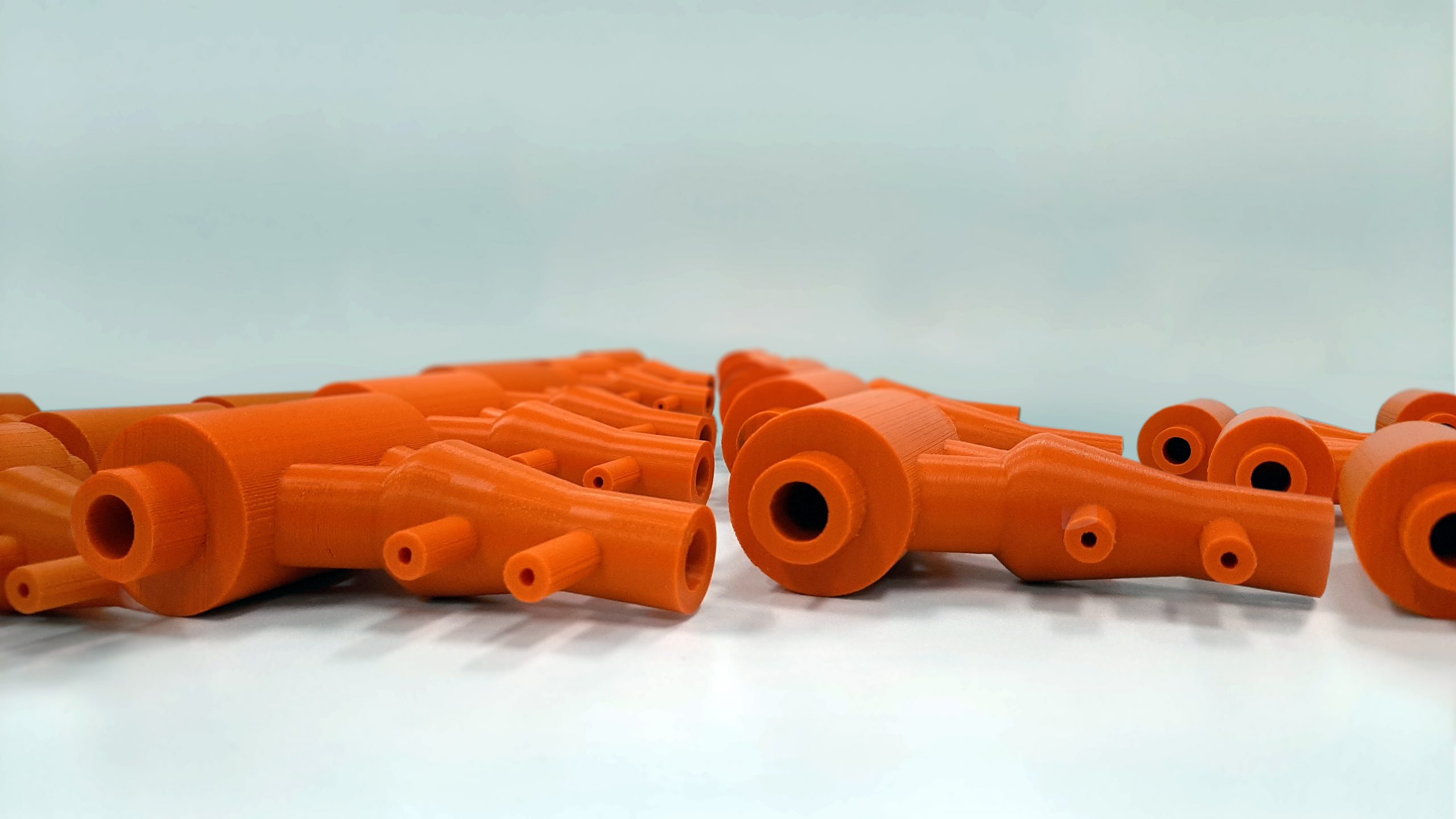 Multiple Orange Post-processed FDM 3D printed parts laying down. 