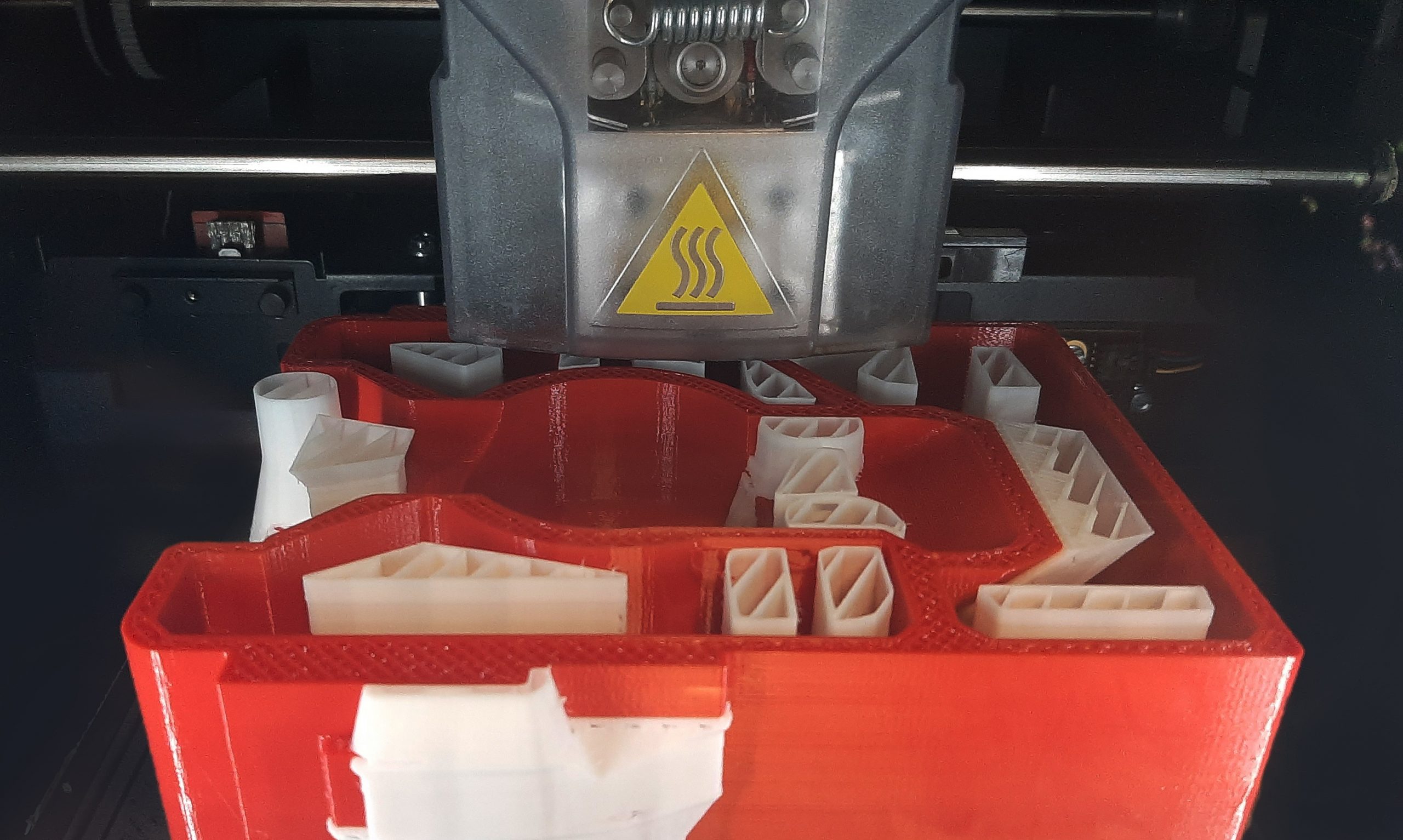 FDM 3D printer printing a red part with white support structure.