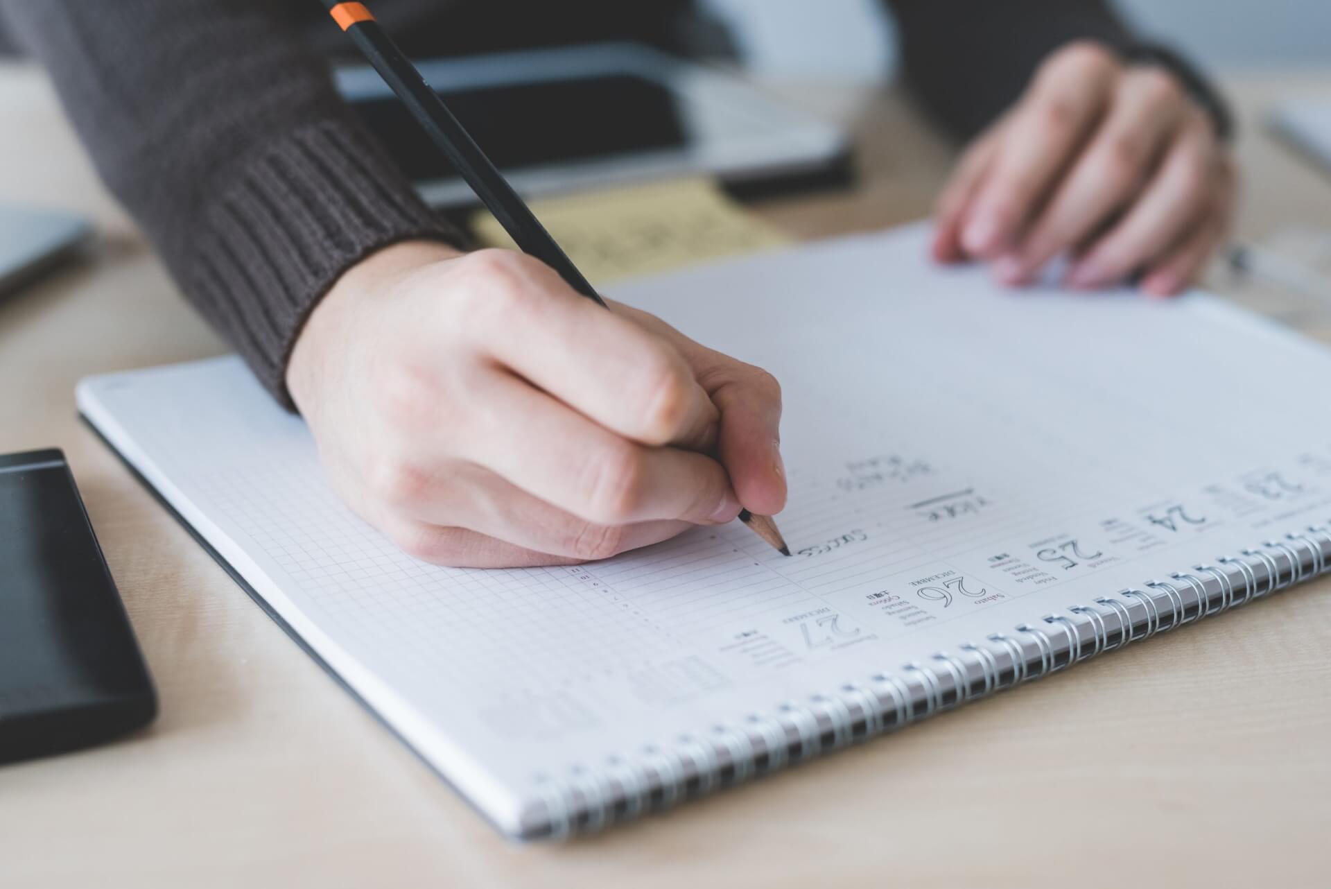 Hand writing with a pencil in on a desk calendar.