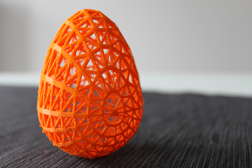 3D printed orange egg with lattice work on black table with grey background.